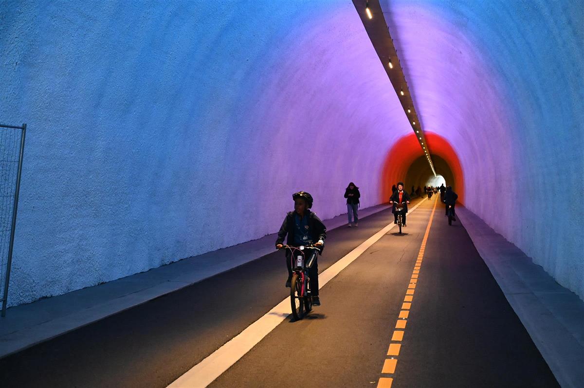 Syklistar i tunnelen med blått og rødt lys i taket. - Klikk for stort bilete